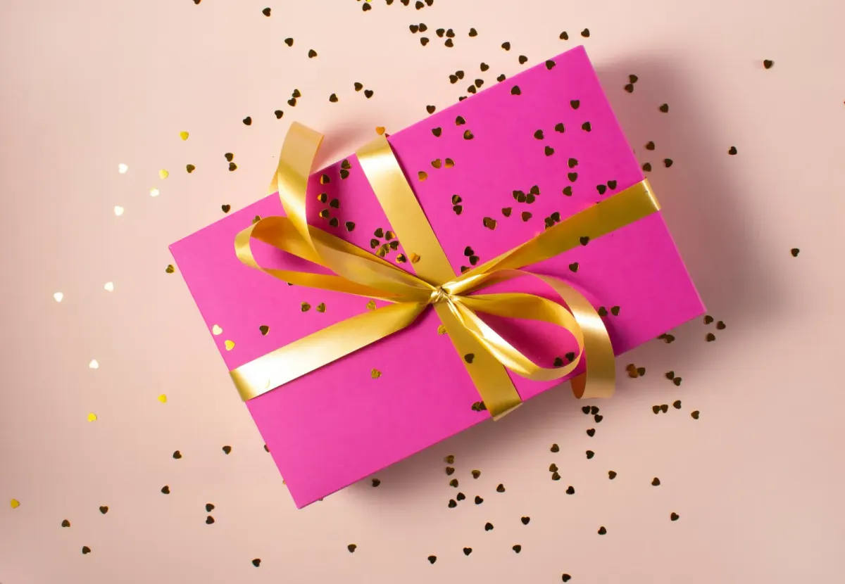Pink gift box wrapped with a gold ribbon and confetti