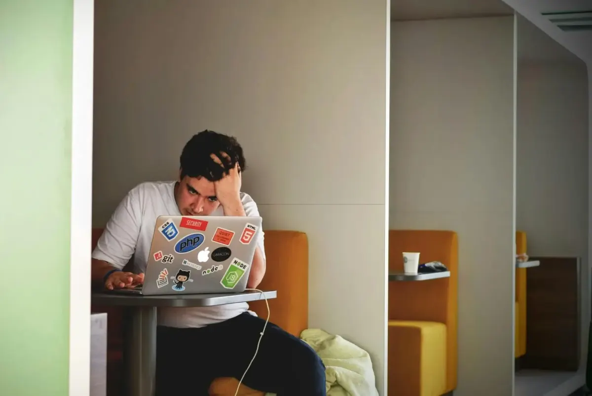 Frustrated student looking at a laptop covered in coding stickers