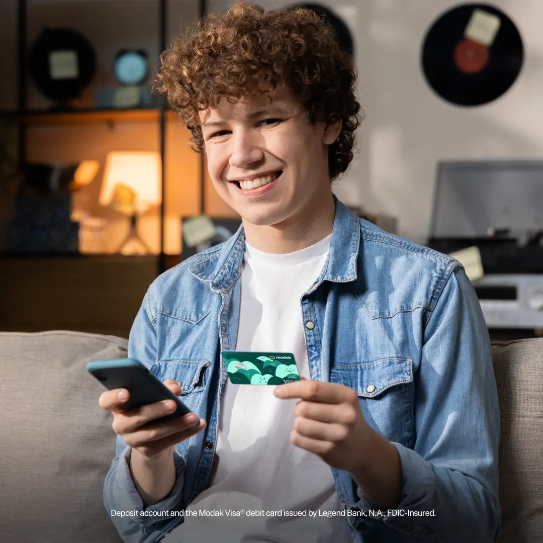 Teen smiling while holding a phone and a Modak debit card