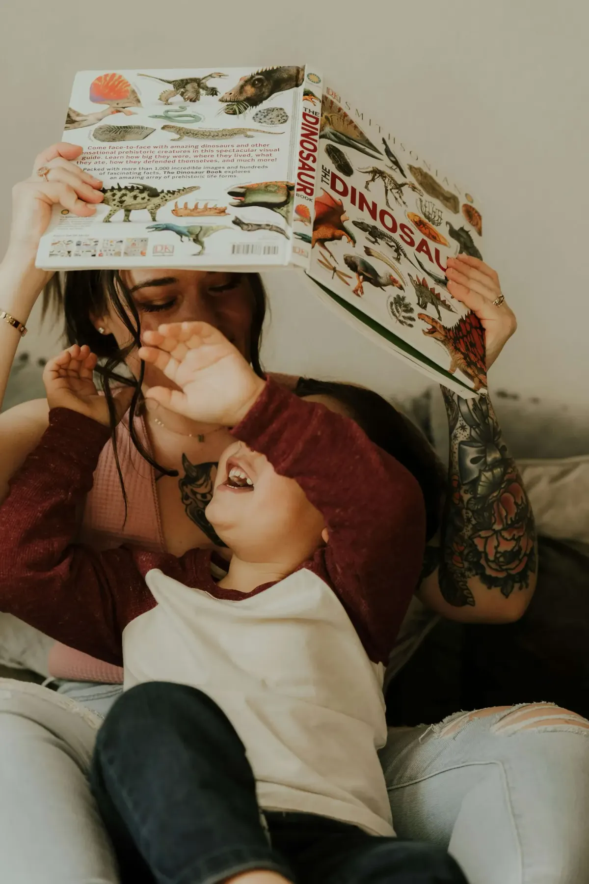 Mother and laughing toddler reading a dinosaur book together