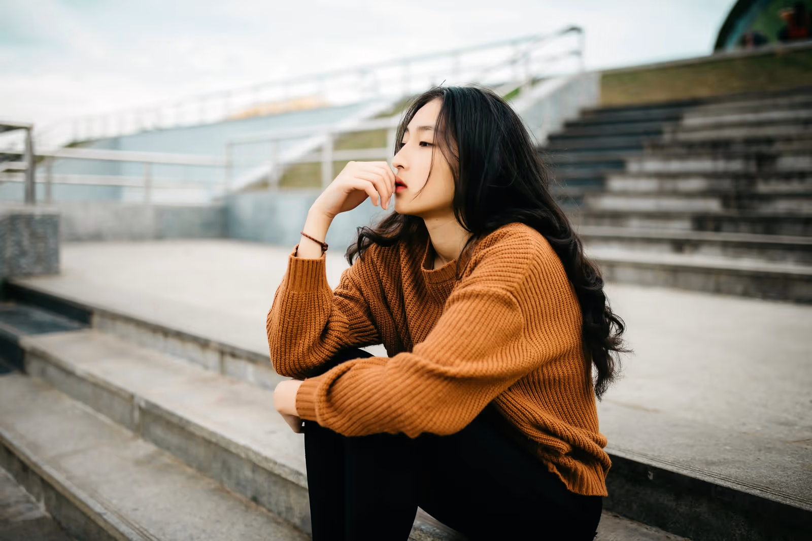 woman in a rust-colored sweater sitting thoughtfully on outdoor steps