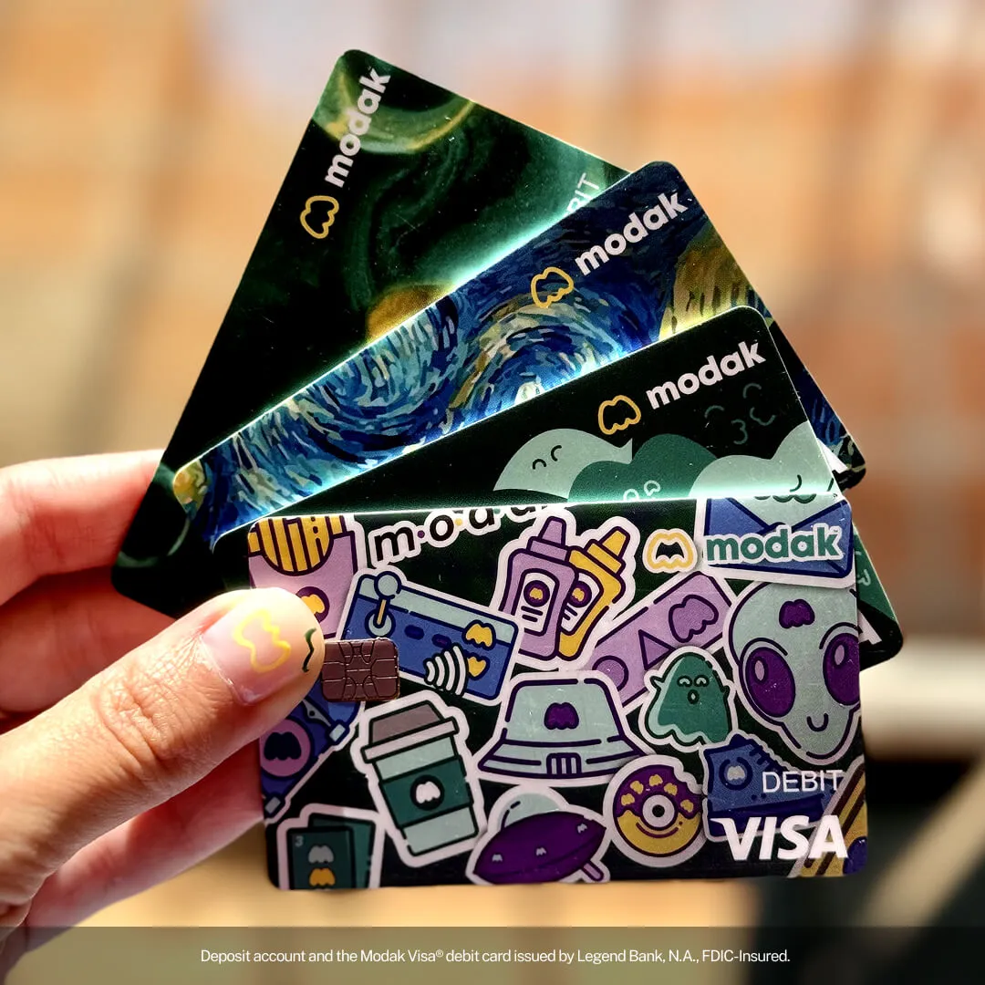 Hand fanning out three Modak debit cards with colorful designs