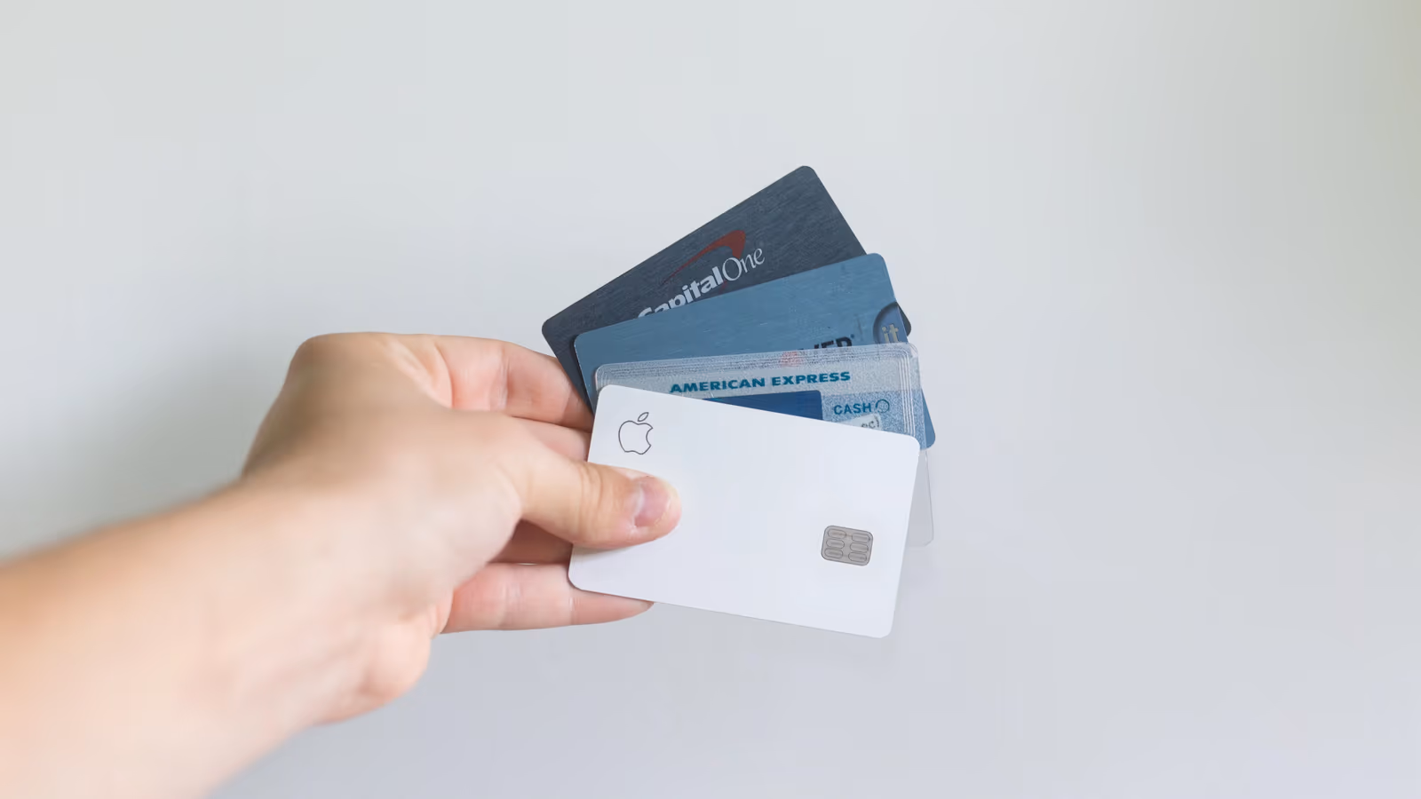 Hand fanning a white Apple Card among Capital One and Amex cards