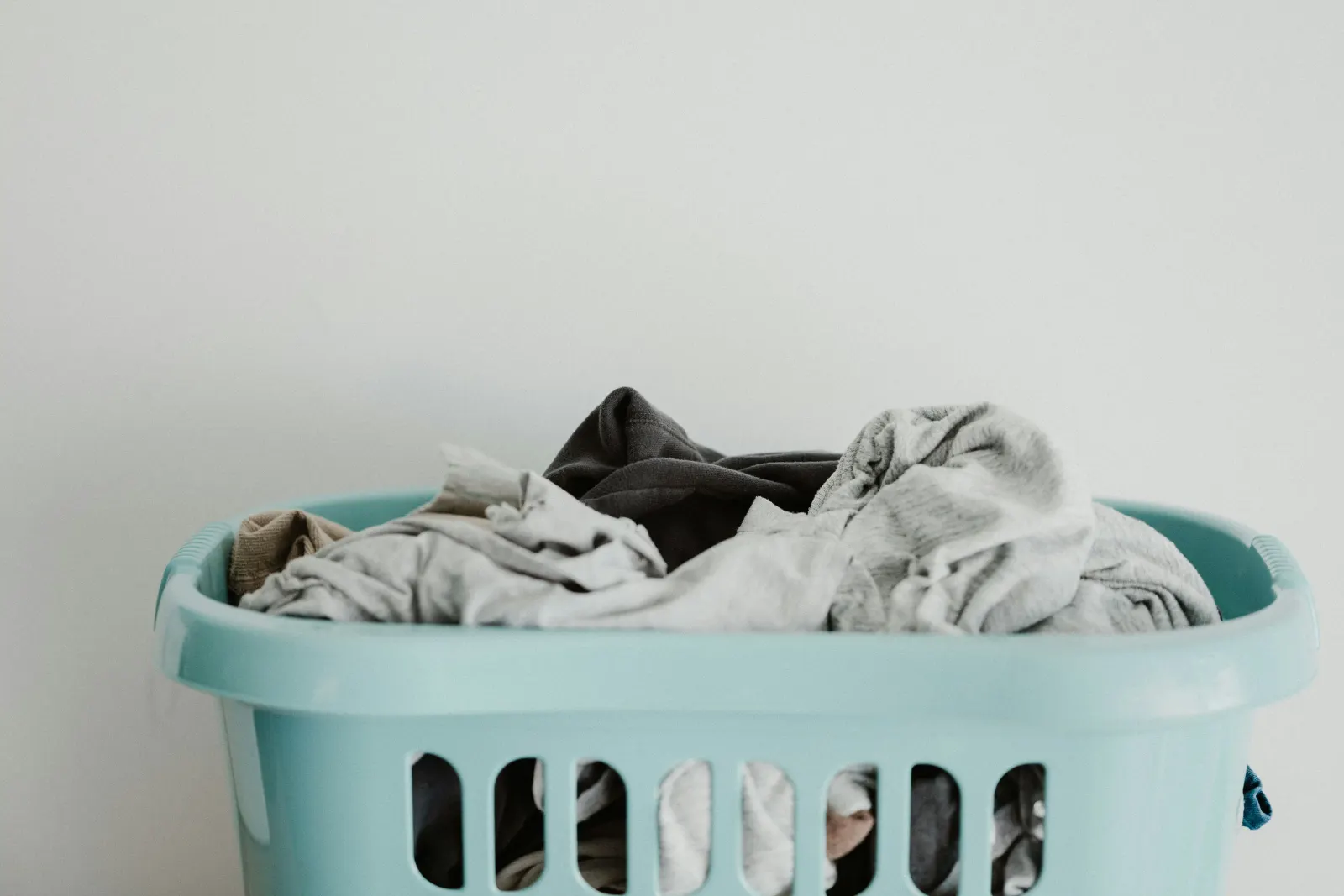 Mint-green laundry basket overflowing with grey clothes