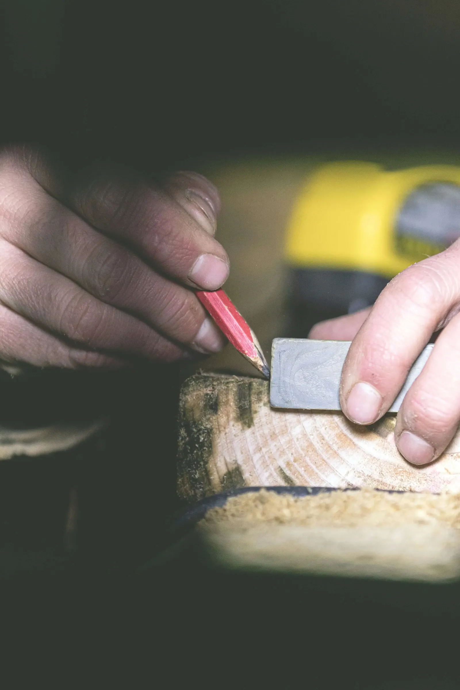 Hands marking a block of wood with a pencil