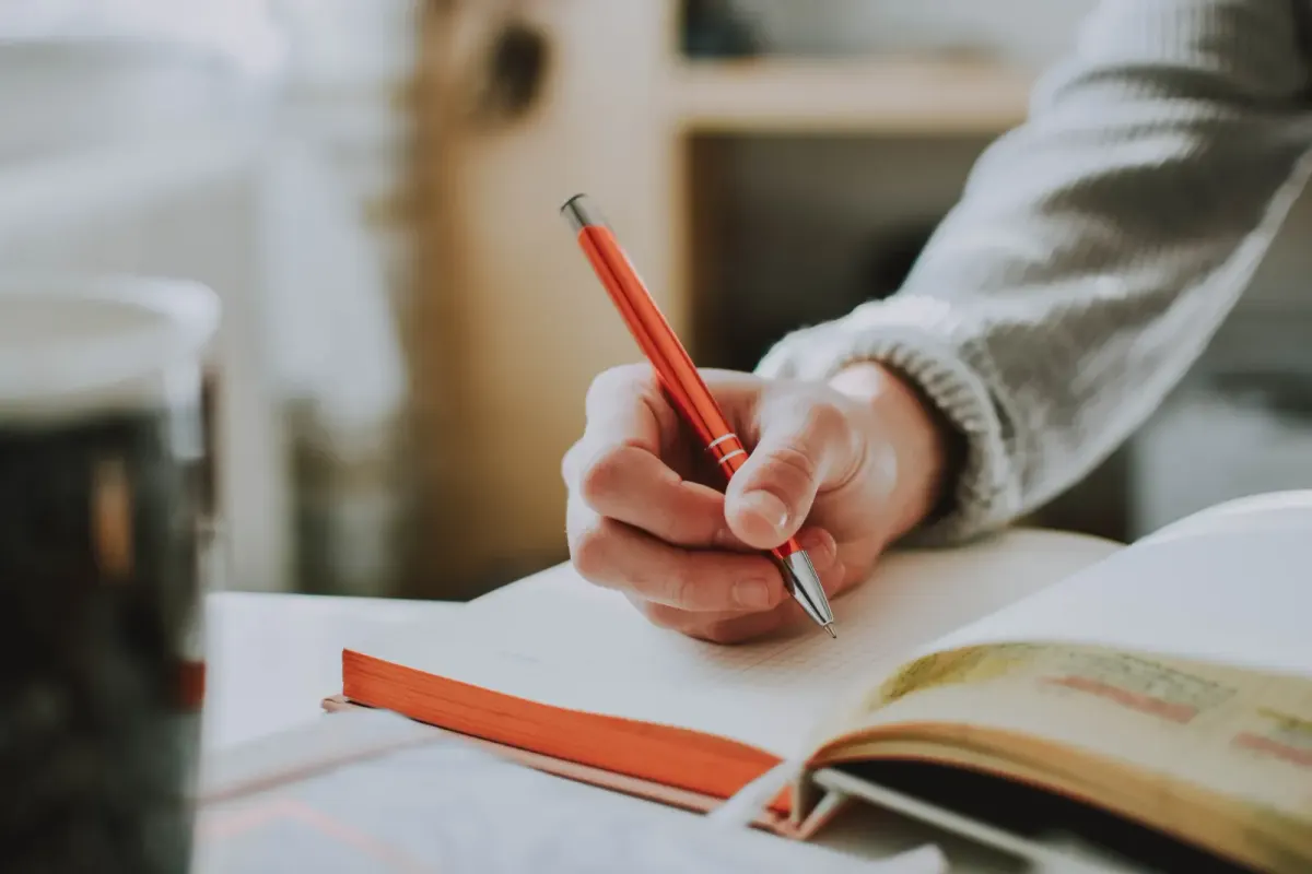 close-up of a hand writing in an open notebook with an orange pen
