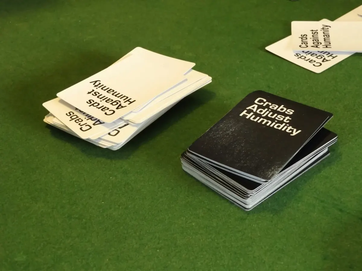 stacks of Cards Against Humanity and Crabs Adjust Humidity card decks on a green surface