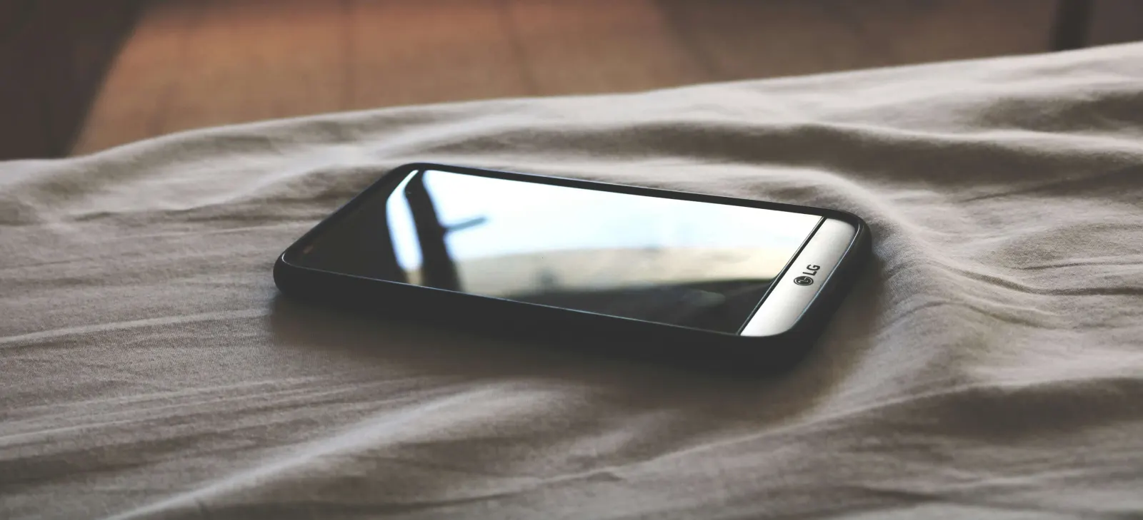 Black smartphone lying face-up on a rumpled bed sheet