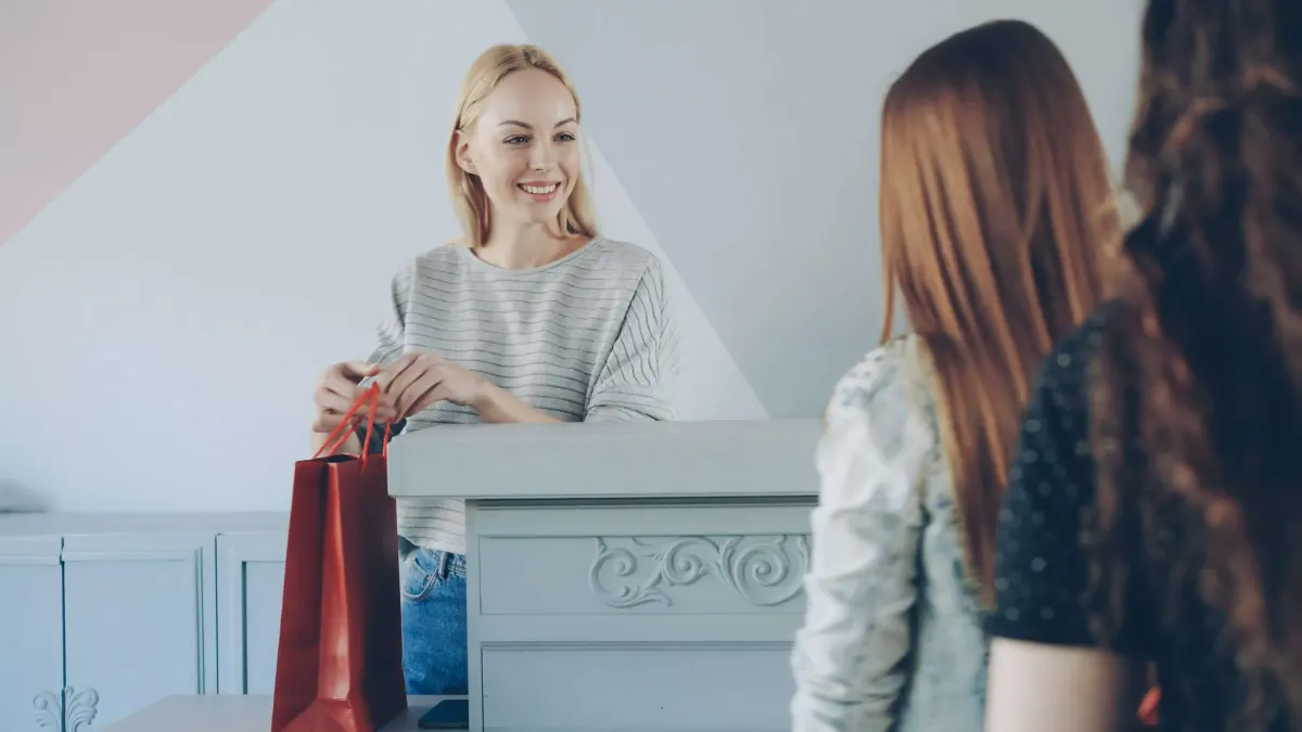 Store employee handing a red shopping bag to a customer