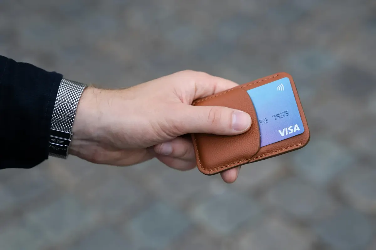 Hand holding a brown wallet with a blue Visa card tucked in