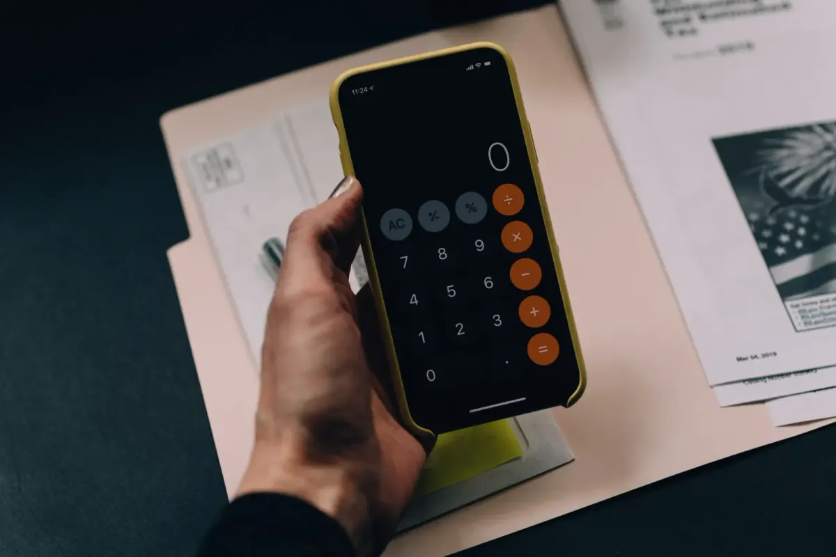 Hand holding a phone showing a calculator app over paper documents