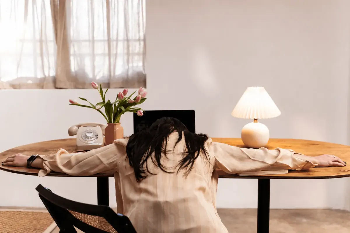 Person resting their head on a desk, arms stretched out, looking bored