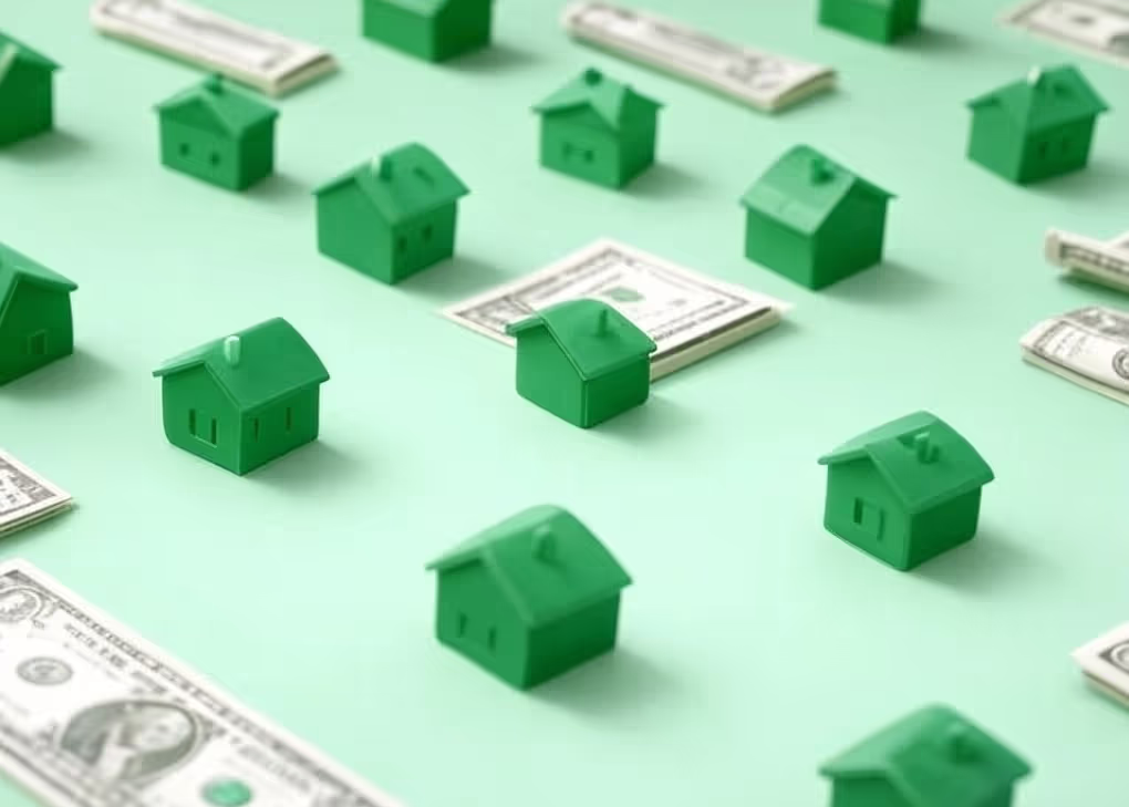 Miniature green houses and folded cash bills on a mint background